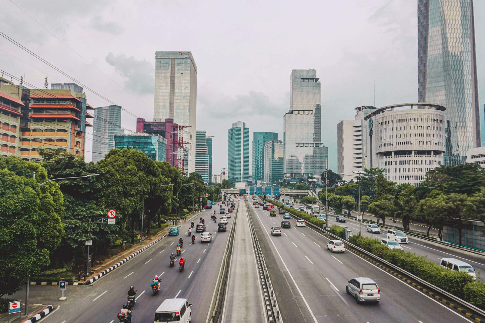 A busy Indonesian city highway with tall buildings in the background.